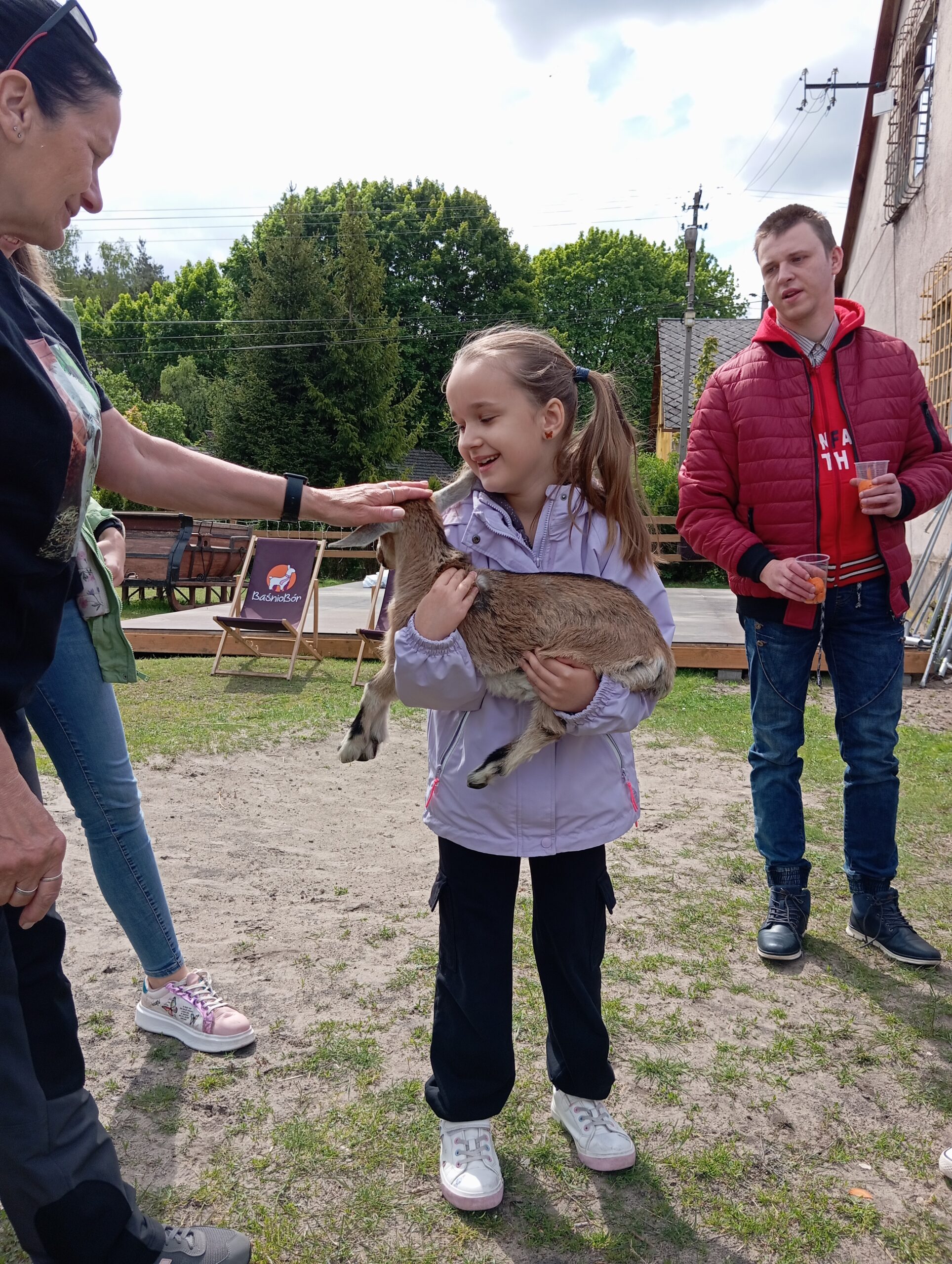Zdjęcie przedstawia dziecko trzymające małą kozę
